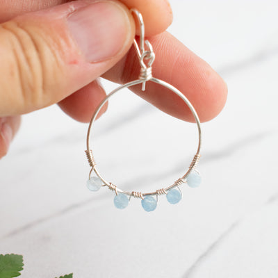 A woman holds a Silver and Aquamarine hoop earring.