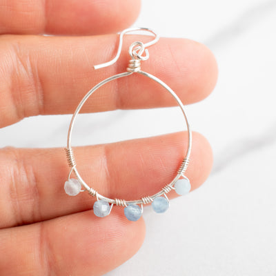 Aquamarine and Silver hoop earring held in a woman's hand.