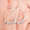 Silver plated hoop earrings with Aquamarine beads held in a hand.