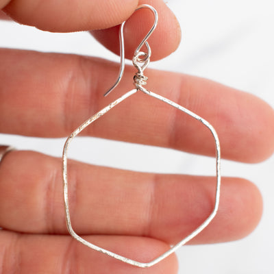 Wire wrapped hexagon earrings shown held in a woman's hand.