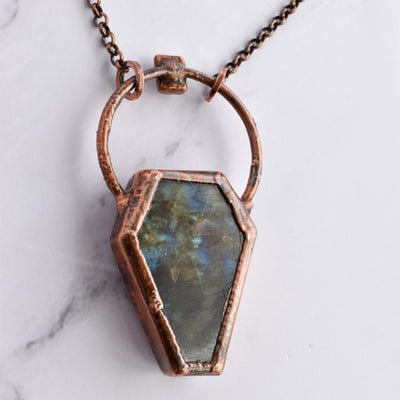 The back of the Labradorite coffin pendant shows blue, yellow and dark green swirling colours. The pendant features a copper bail, and hangs on a pure copper rolo chain.