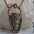 Light glints off the rose cut facets of a Labradorite coffin pendant featuring flashes of blue, green yellow and pinky-purple. A rainbow moonstone oval accents the top of the copper bail, and hangs on a pure copper rolo chain displayed in front of a Quartz crystal.