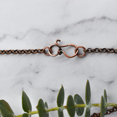 Copper rolo chain with a wire wrapped infinity clasp. Green eucalyptus leaves are arranged below the chain.