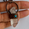 A Clear Quartz point crystal is encircled with antique copper and accented with a small hexagonal blue flash Labradorite stone. The necklace is held in a human hand.