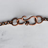 Light reflects off the texture on a handmade wire infinity loop clasp and rolo chain.