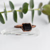 A Black Tourmaline ring is set in antique copper, the ring is placed on top of a Quartz point and in front of green eucalyptus leaves.