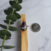 Copper and Chevron Amethyst ring is displayed on a Palo santo stick of wood. A quarter coin and eucalyptus branch are displayed beside the ring.