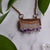 Shiny copper frames an Amethyst slice pendant. The banded layers show the crystal formation from brown and cream Agate to clear Quartz to sparkly purple and clear points. Pendant hangs from bright copper chain. Green leaves are arranged around necklace.