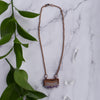 Shiny copper frames an Amethyst slice pendant. The banded layers show the crystal formation from brown and cream Agate to clear Quartz to sparkly purple and clear points. Pendant hangs from bright copper chain. Green leaves and Quartz points are arranged around necklace.