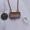 Shiny copper frames an Amethyst slice pendant. The banded layers show the crystal formation from brown and cream Agate to clear Quartz to sparkly purple and clear points. Pendant hangs from bright copper chain. A quarter coin and Quartz point are placed beside pendant to reference the size.