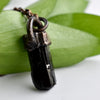 A Black cylindrical Tourmaline stone and antiqued copper pendant is arranged over green leaves.