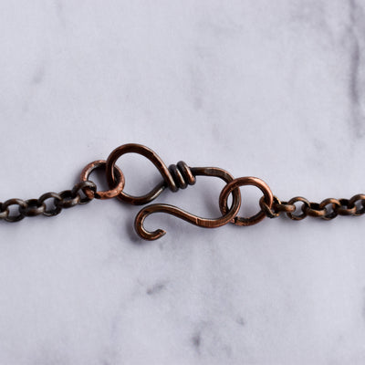 Light reflects off a hand wire wrapped copper infinity loop clasp and rolo chain.