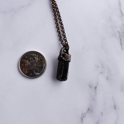 Black Tourmaline and copper necklace arranged beside a Quarter coin for size reference.