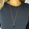 A Black Tourmaline pendant hangs from a copper chain. \the necklace is worn by a woman in a black shirt. The necklace hangs below the bust.