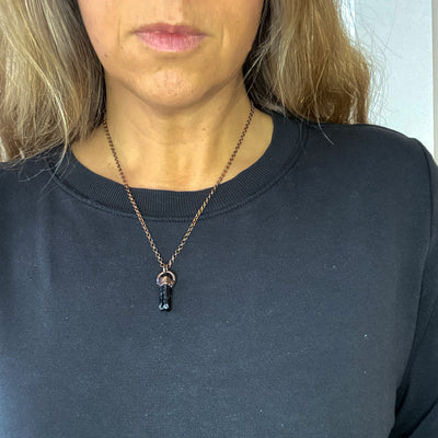 A Black Tourmaline and copper necklace is worn by a woman in a black shirt.