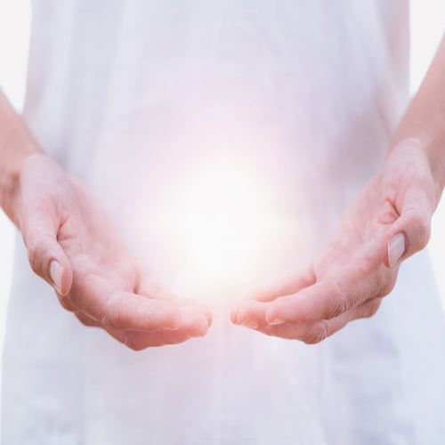 Outline of a body in the background with hands in the forefront raised upwards an light is pictured in the palms of the hands.